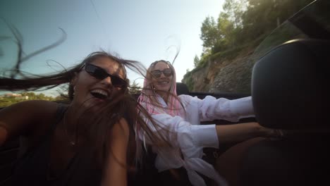 two joyful women on a convertible road trip, hair blowing in the wind, taking selfies