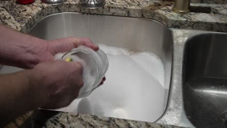 a man washes a cup with a sponge in a sink of bubbles