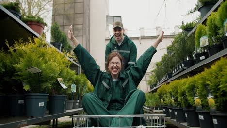 Diversión-En-Invernadero:-Trabajadores-Transportando-Plantas-En-Un-Carro-Con-Una-Chica-Alegre-Agitando-Las-Manos