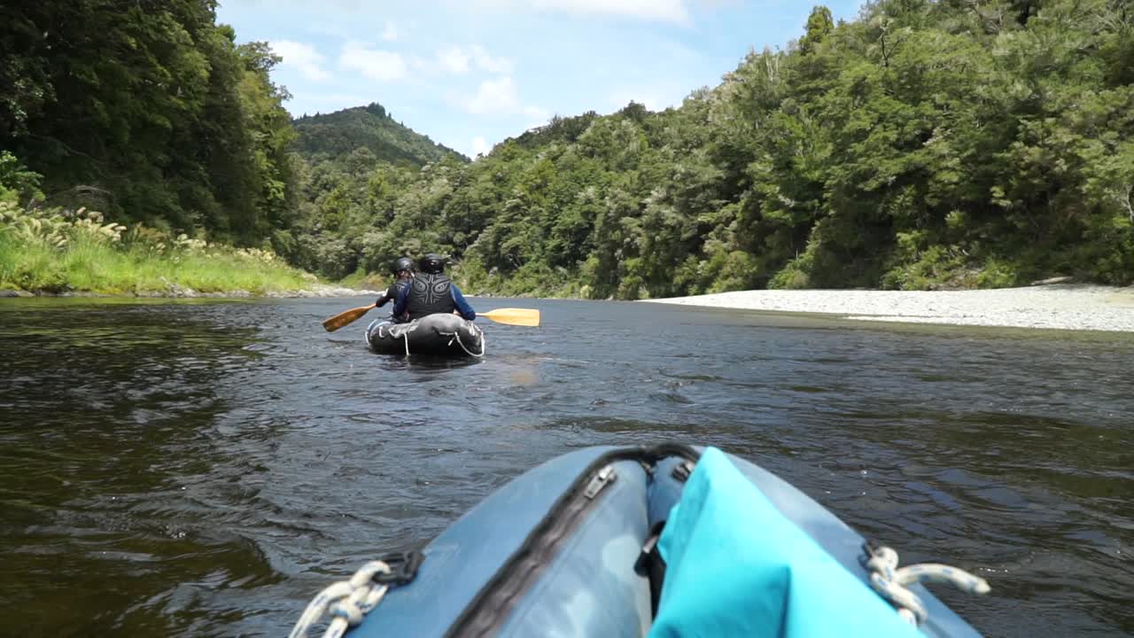 cámara lenta: dos personas reman en canoas, un hermoso río azul prístino y claro, nueva zelanda, con un exuberante bosque nativo en segundo plano.
