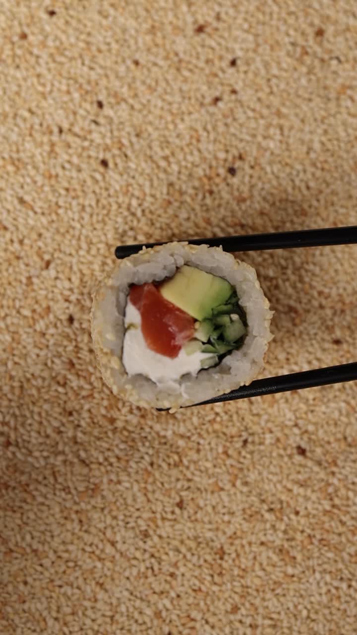 Lähikuva syömäpuikoilla pidetystä California-rullasta