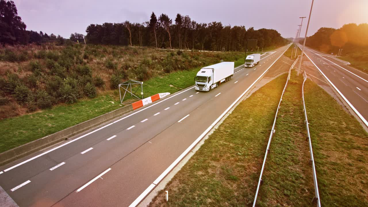 Camion commerciali con rimorchio merci percorrono un'autostrada deserta. Il sole splende sullo sfondo
