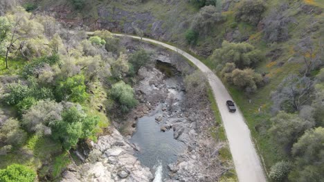 Pickup-truck-driving-by-a-river-bend-in-the-mountains-on-a-dirt-road