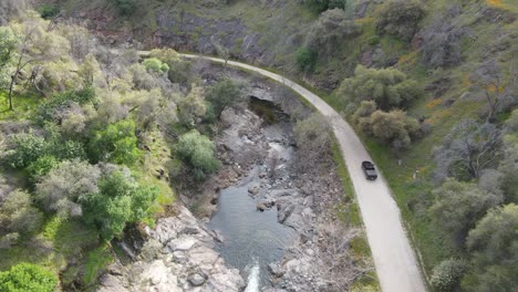 camioneta conduciendo por una curva del río en las montañas en un camino de tierra