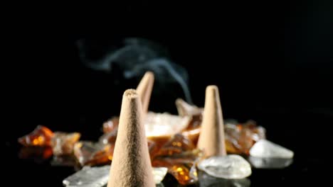 empujando lentamente varios conos de incienso apagados en un jardín de rocas decorativas, hacia un cono iluminado con humo ondulante