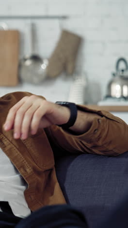 young freelancer rests on sofa. tired man puts his laptop off while sitting on the couch at home. difficult remote job during coronavirus. vertical video