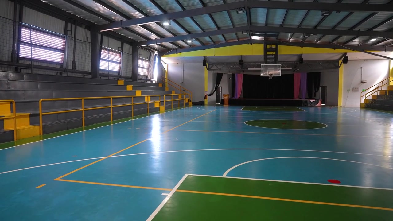Filmaufnahmen einer Sporthalle in einer Bildungseinrichtung mit Sportinfrastruktur, sportlicher Trainingsumgebung und schulischen Freizeiteinrichtungen.