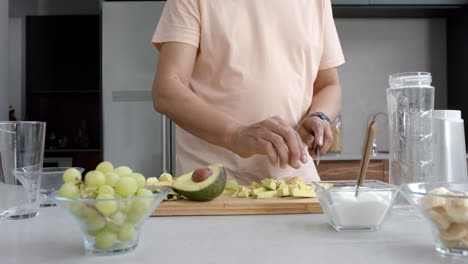 midsection of senior biracial man chopping fruit and vegetables for smoothie in kitchen, slow motion