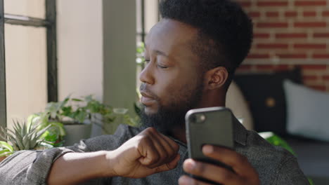 portrait young african american man using smartphone at home browsing messages networking texting social media sharing lifestyle online planning ahead in modern apartment close up
