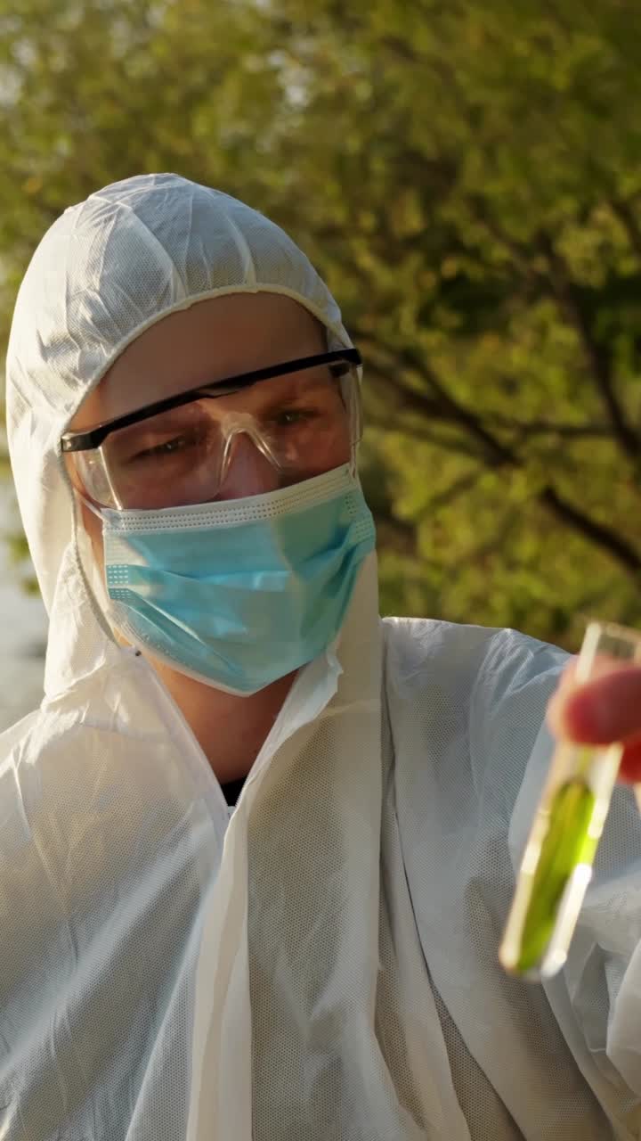 Masked environmental inspector holding water sample with leaf in test tube bottle while conducting safety check outdoors