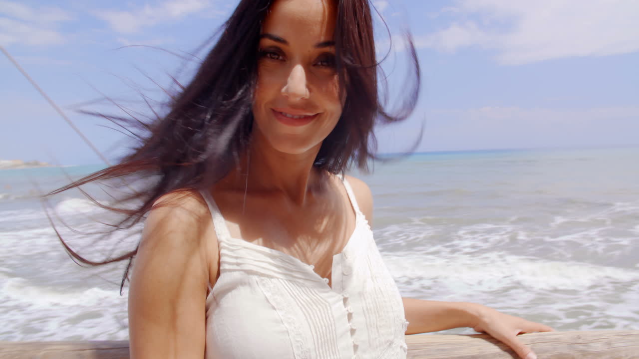 해변에 있는 여자가 카메라를 보고 웃고 있다.