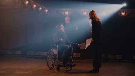 actors with script acting out argument with director woman with script arguing with man on wheelchair while rehearsing quarrel scene near aged director on stage in theater