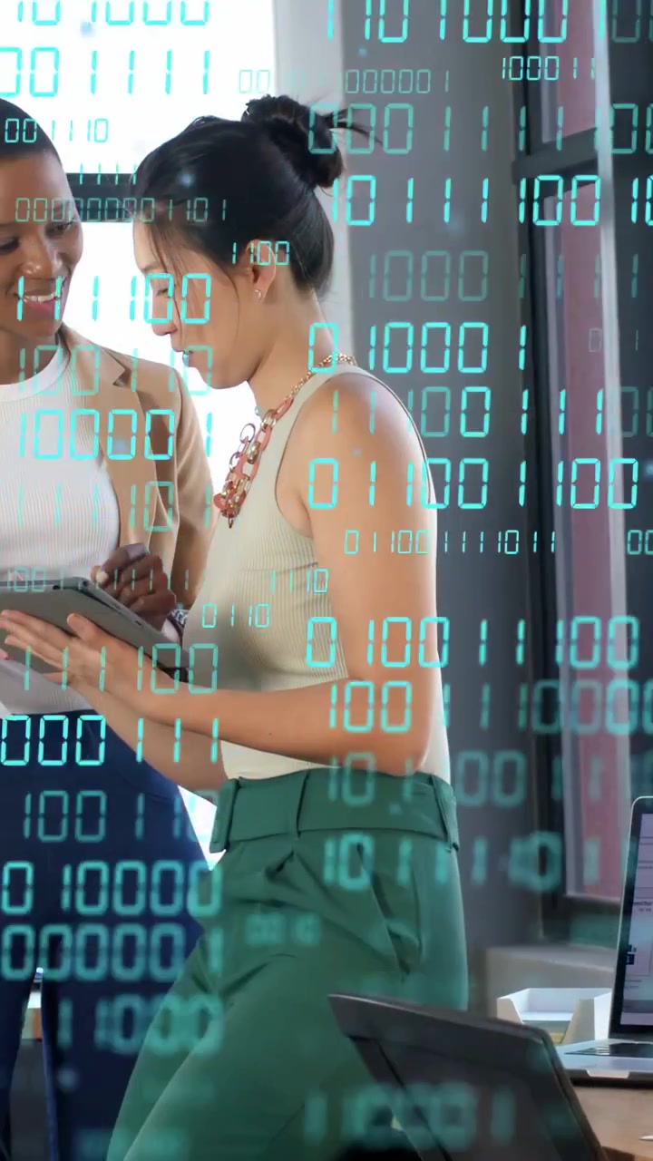 Vertical video: Woman tapping tablet, leaning while peer watching, binary overlay showing tech data