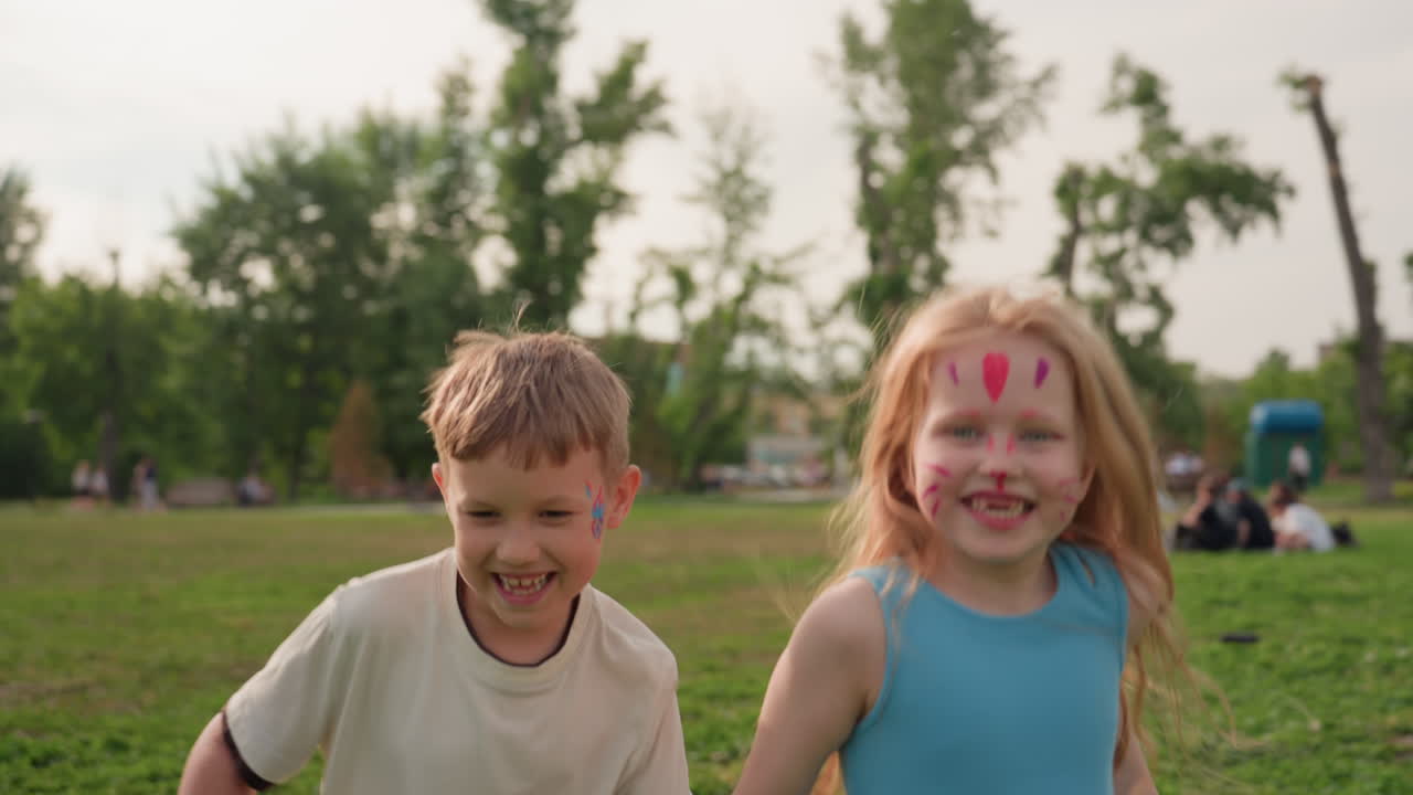 Crianças alegres correndo com sorrisos nos rostos na grama verde do parque, de mãos dadas, vento nos cabelos, energia brincalhona, tarde de verão, movimento alegre, infância despreocupada ao ar livre.