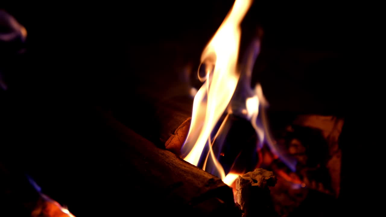 Warm cozy burning fire in fireplace. Burning fire and flames on black background. Flames and burning sparks. Fire patterns. Glow of fire in the dark with copy space. Close-up shot.