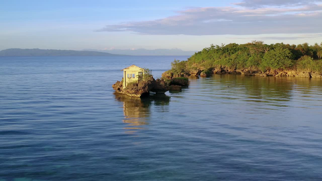 Ruins of an old house on an offshore island of a Mediterranean coastal landscape in the light of the setting sun. Panoramic drone view