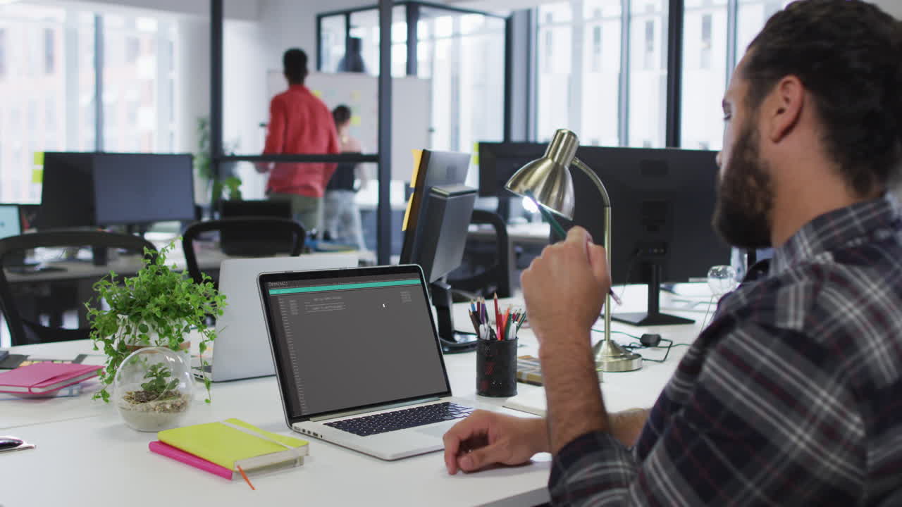 Caucasian man sitting at desk watching coding data processing on laptop screen