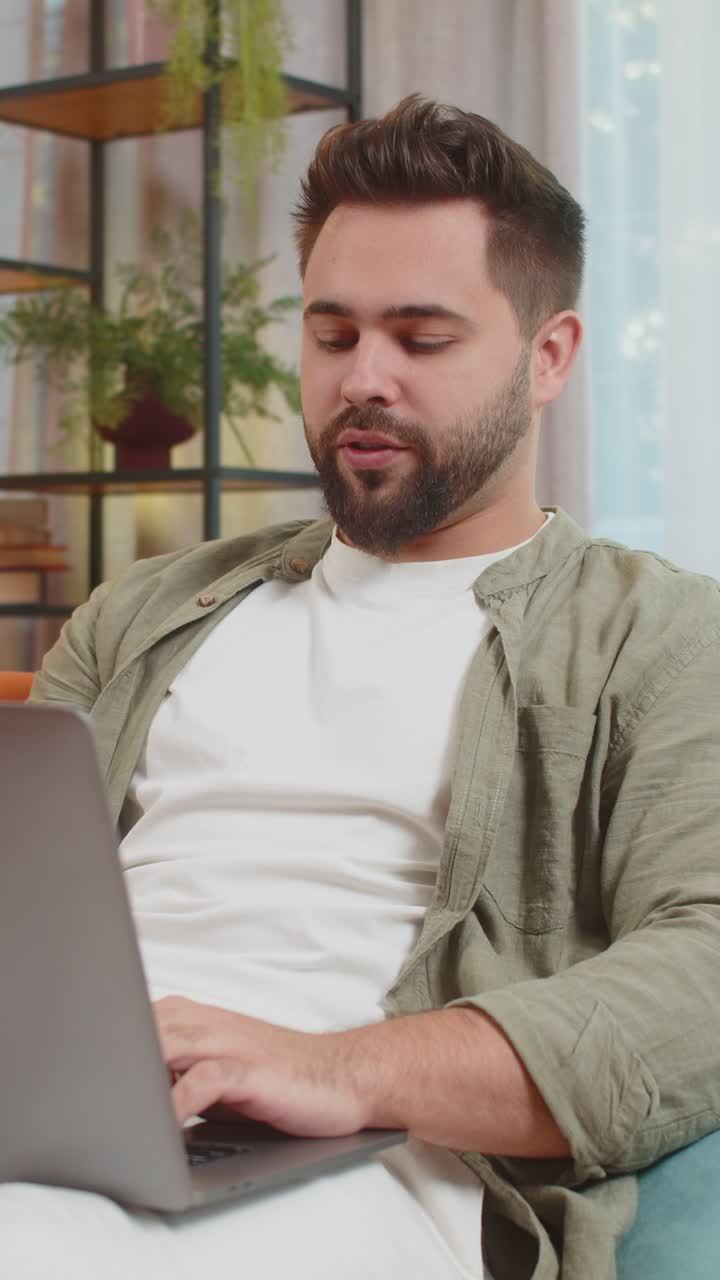 Confident young man on sofa couch using laptop making an online video conference call in distance