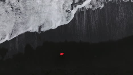 bird's eye view of a person on the shore of reynisfjara black beach with foamy waves in iceland