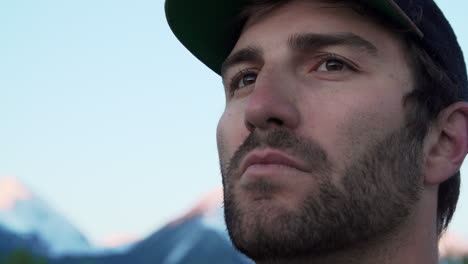 extreme close up of an outdoorsman millennial looking on as the sun just begins to cast a pink glow on the snow-capped mountains in the background