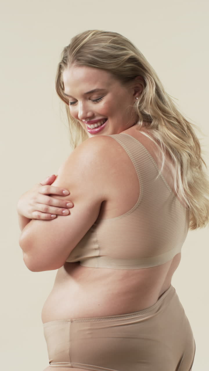 Vertical video: Smiling plus size woman in beige underwear embracing body positivity