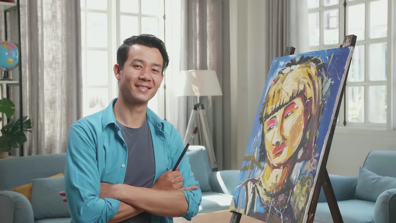 Medium Shot Of An Asian Artist Man Holding Paintbrush Mixed Colour, Crossing His Arm, And Smiling After Finish Painting A Girl On The Canvas