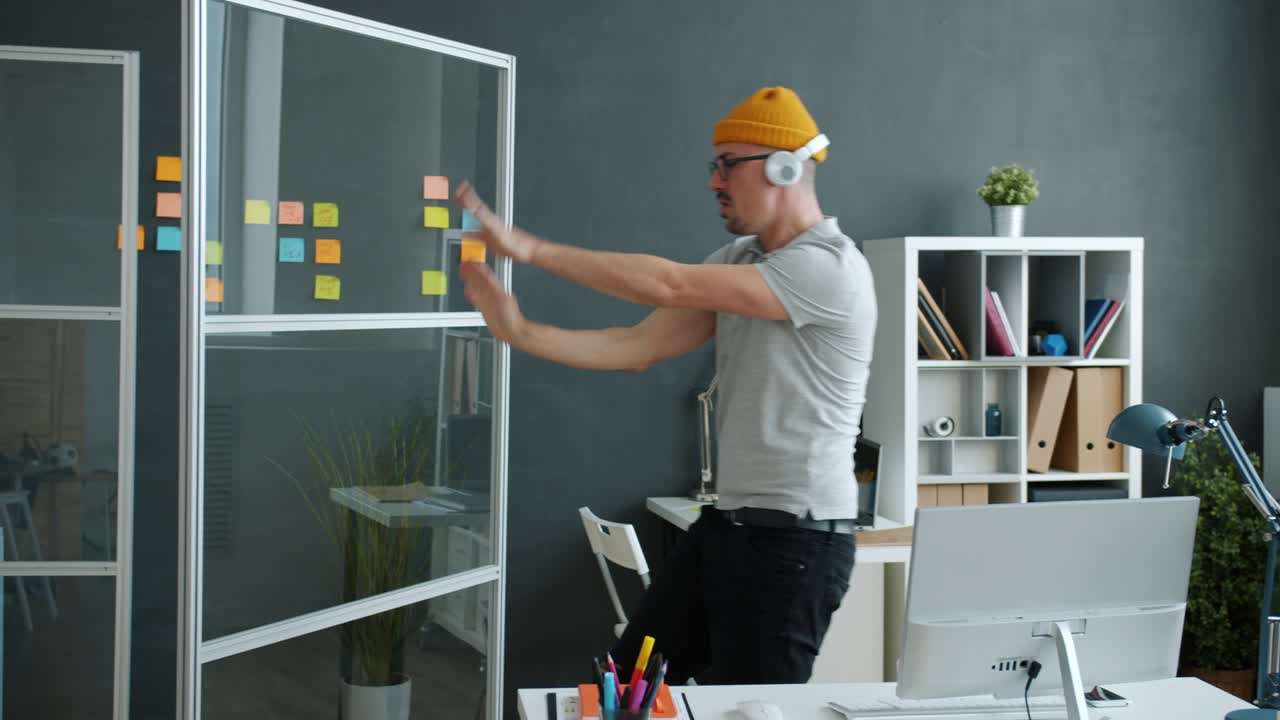 Carefree employee having fun in workplace dancing wearing headphones