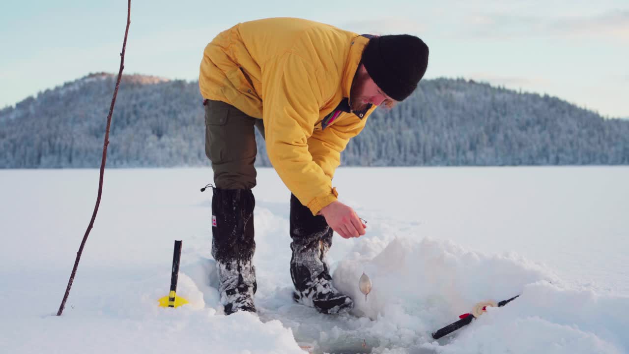 hombre agachándose, usa cebo en caña de pescar para atrapar peces en un agujero de hielo