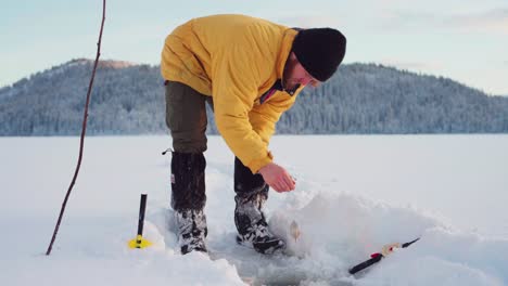 man bending down, uses bait in fishing rod to catch fish in ice hole