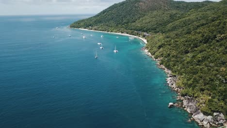 Panorámica-Aérea-De-Drones-Sobre-Una-Isla-Forestal-Tropical-De-Aguas-Azules-Claras-Con-Barcos