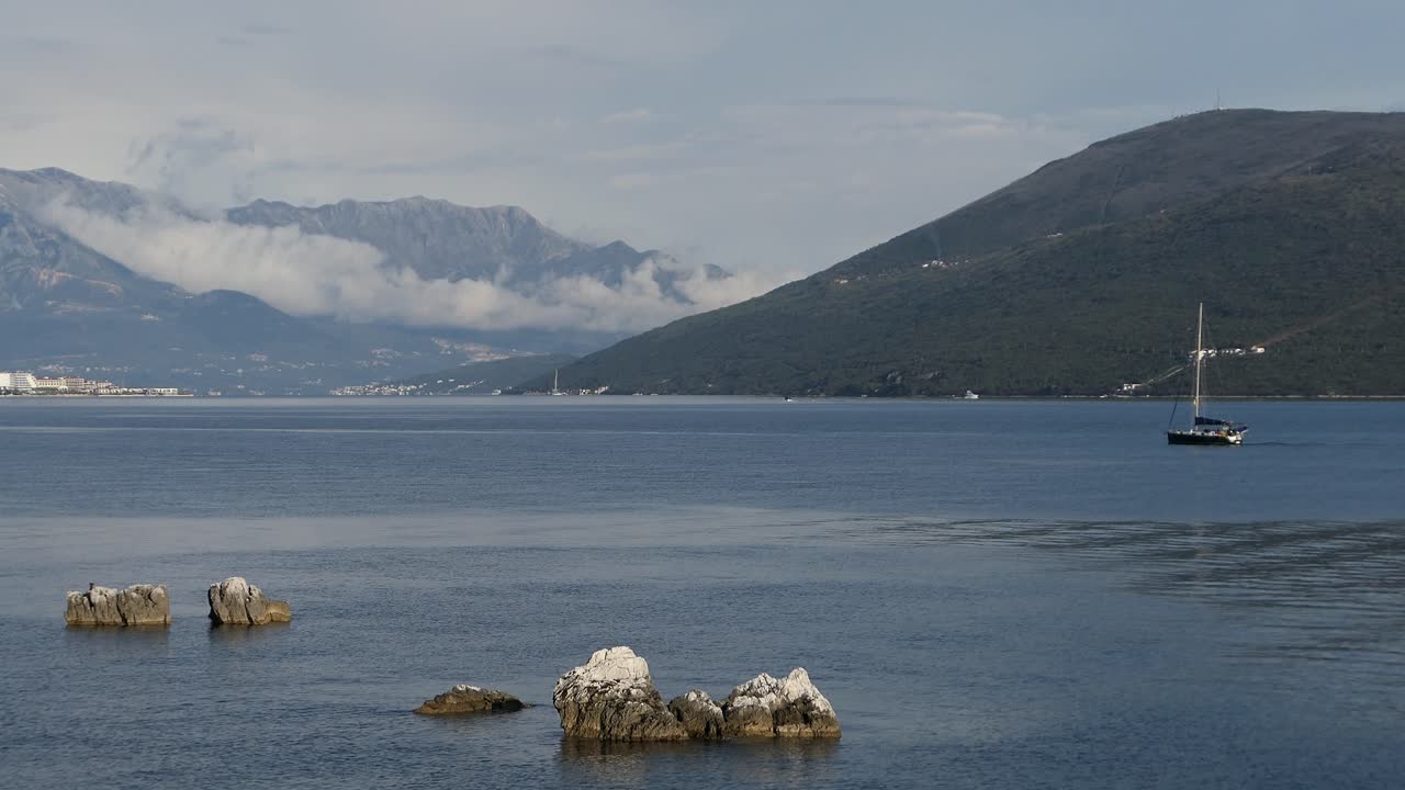 Calm sea with sailboat and clouds around mountains, Kotor Bay area, Montenegro