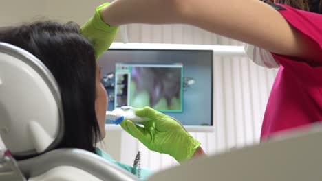 Young-female-dentist-examining-the-mouth-of-a-patient-with-an-intraoral-camera-and-showing-image-on-the-screen.-Shot-in-4k