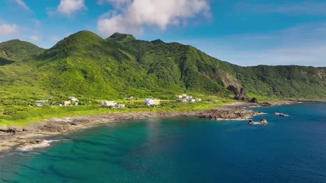 Cinematic-drone-shot-of-luxury-buildings-on-green-Orchid-Island-and-turquoise-pacific-ocean-in-foreground-at-golden-hour