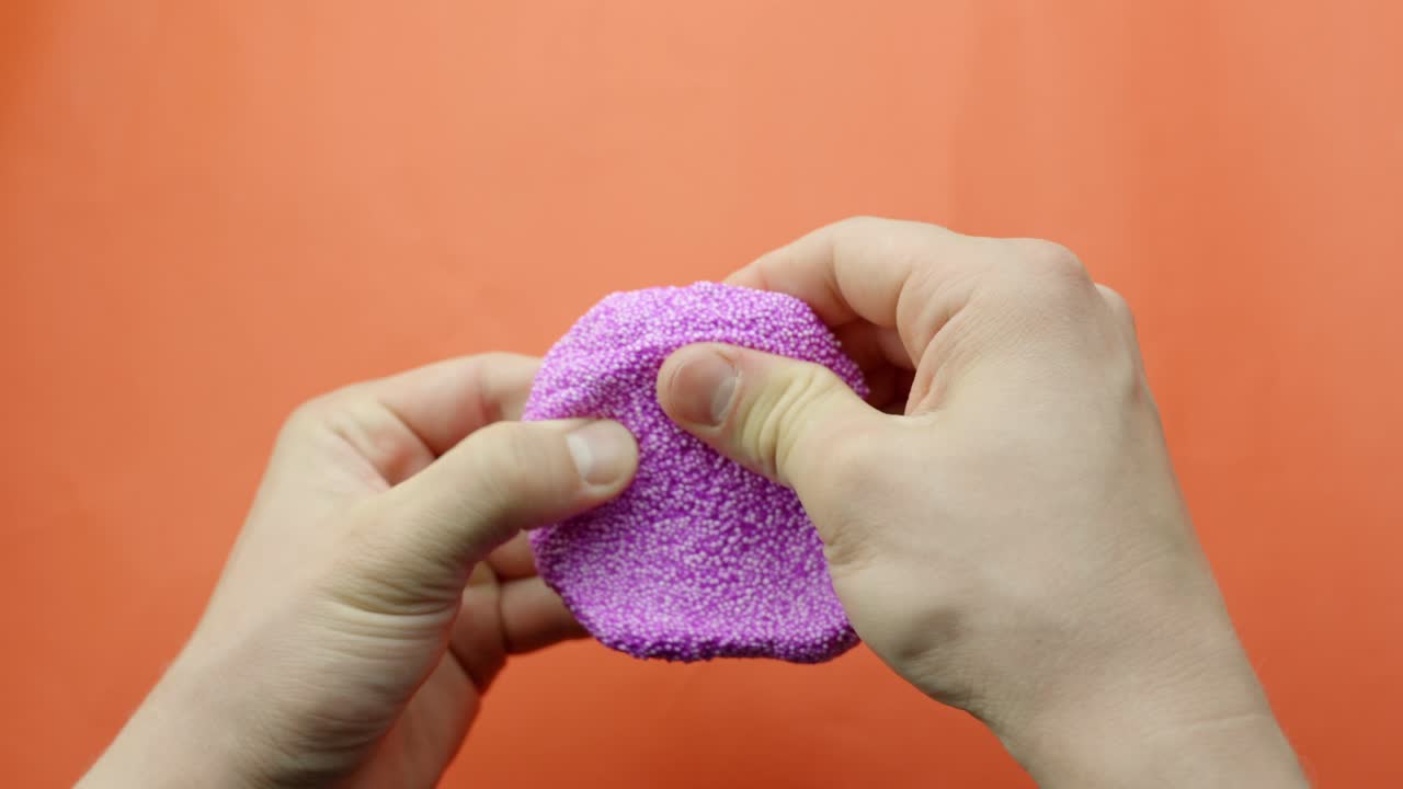 Person manipulating purple foam slime over orange background, pov