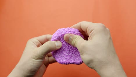 person manipulating purple foam slime over orange background, pov