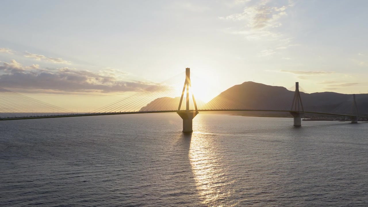 Ponte Rion-Antirion, Grecia. Panoramica con drone al tramonto. Il ponte è drammaticamente in silhouette. Il sole si nasconde dietro i piloni, creando un effetto cinematografico in controluce