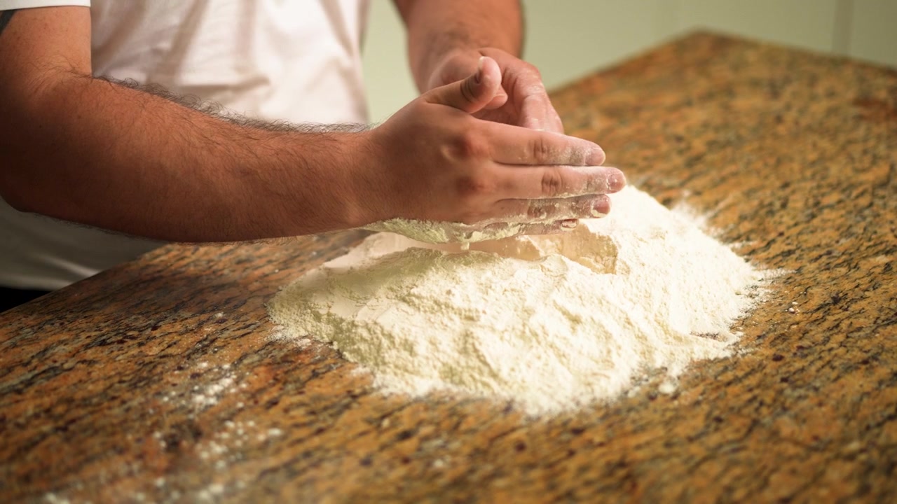 La farina viene cosparsa su un piano di lavoro da uno chef, preparando il terreno per la creazione di una base per pizza perfetta.