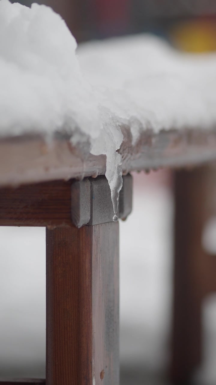 Melting Icicle Dripping Water from a Snow-Covered Wooden Bench