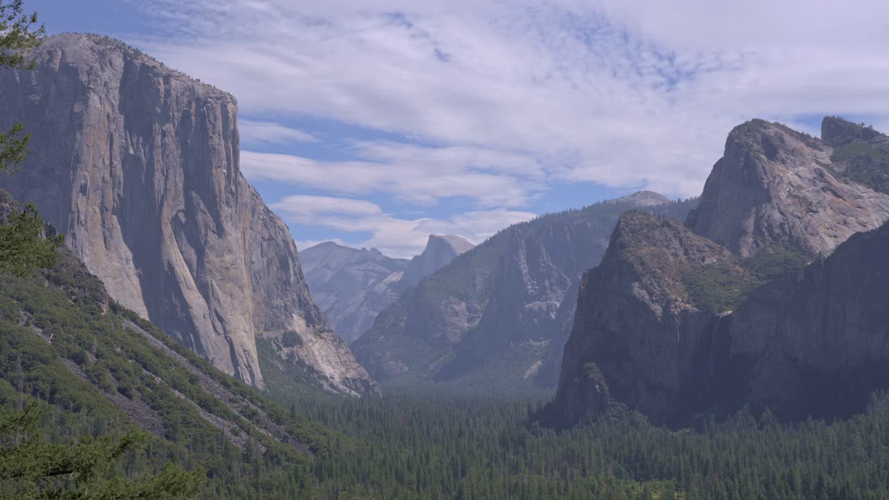 Footage of a medium shot from the famous Tunnel View overlook in Yosemite National Park, California, featuring the iconic granite cliffs of El Capitan and the distant peak of Half Dome.