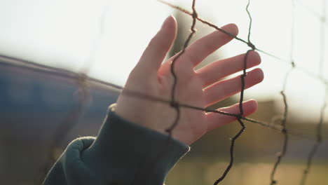 close up hand view of person in green long sleeve gliding hand over volleyball net under golden sunlight rays, blurred background featuring volleyball court