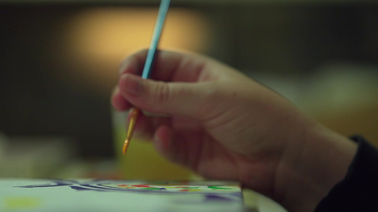 Female hand holding paintbrush as it paints on a colourful canvas. Close up
