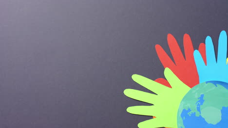 close up of hands together with globe made of colourful paper on gray background with copy space