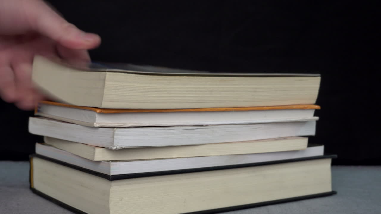 A person stacking books on a table against a black background.