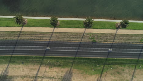 Two-white-vehicles-moving-smoothly-along-Albert-Park-Lake-famous-city-circuit-track-under-afternoon-light