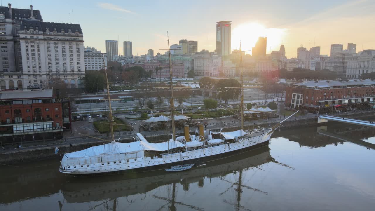 Museum Ship Of ARA Presidente Sarmiento Moored In Puerto Madero, Buenos Aires, Argentina With Backlit Sunlight. aerial pullback