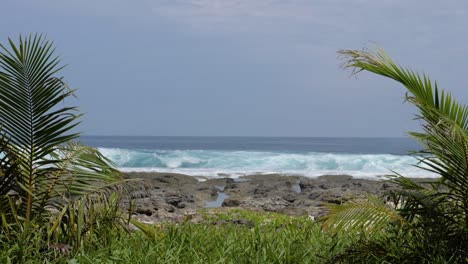 Ultra-slow-motion-shot-waves-coming-in-behind-rocks-at-Asu-Island,-North-Sumatra,-Indonesia