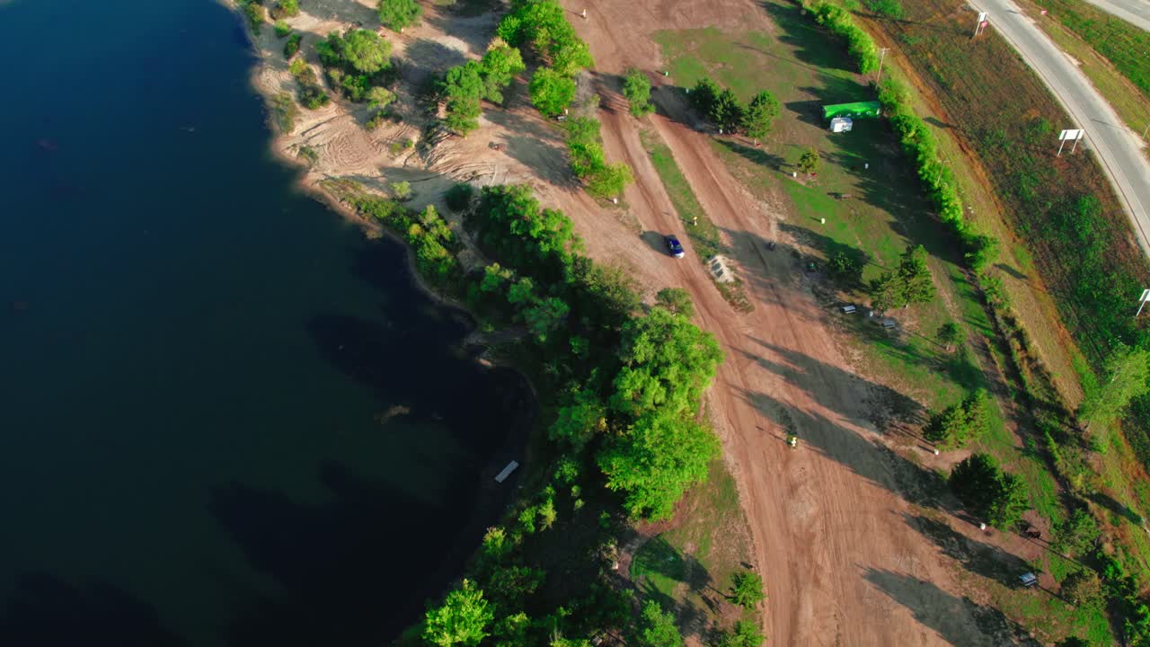 un drone aéreo de arriba hacia abajo sigue a dos bicicletas de motocross mientras aceleran alrededor de un circuito de motocross junto a un pintoresco lago en los estados unidos, estados unidos