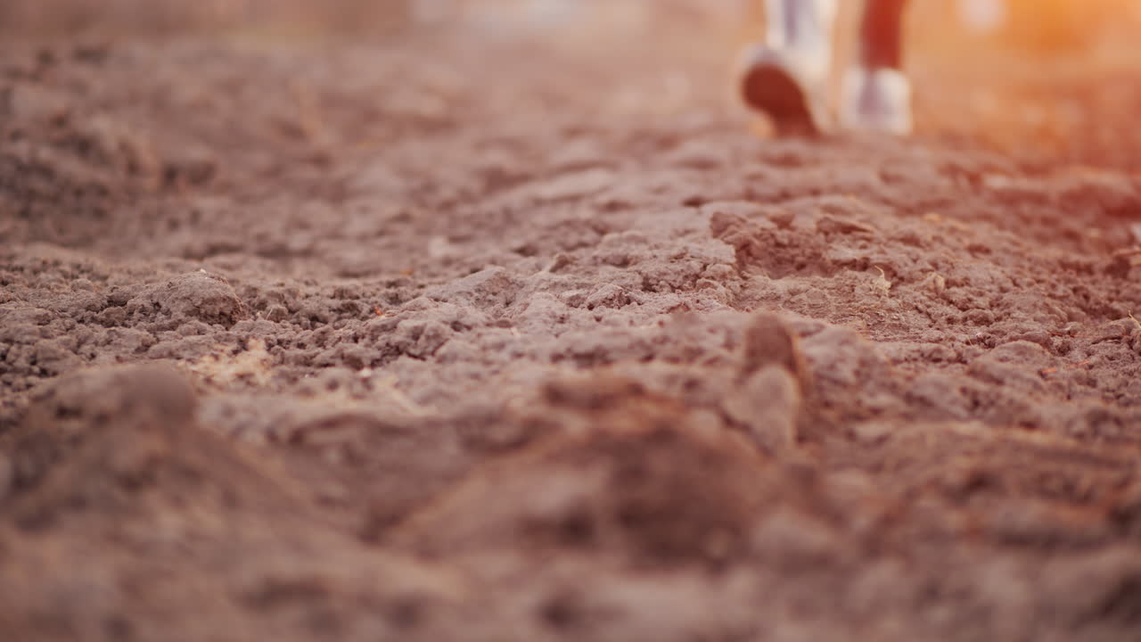 장화를 신은 농부가 경작된 들판을 가로질러 걷고 있습니다. 프레임에는 다리만 보입니다.