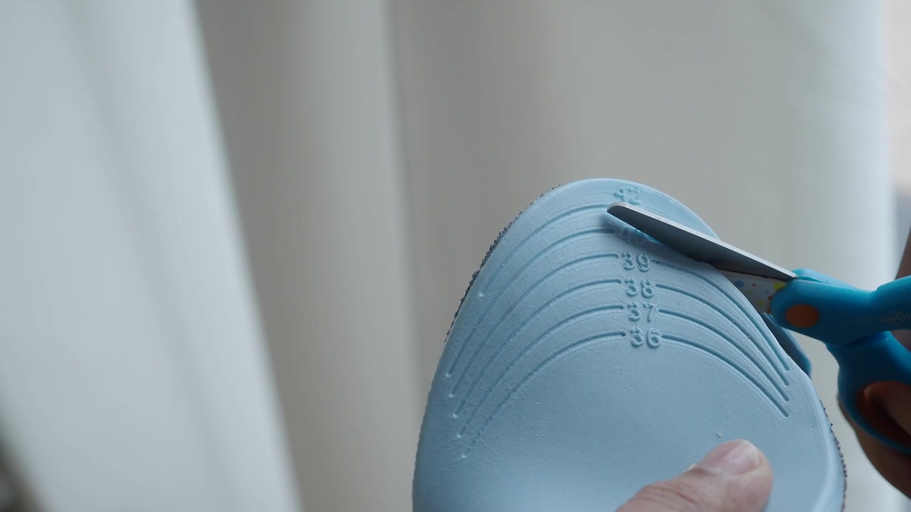 Person Cutting a Shoe Insole to Size with Scissors