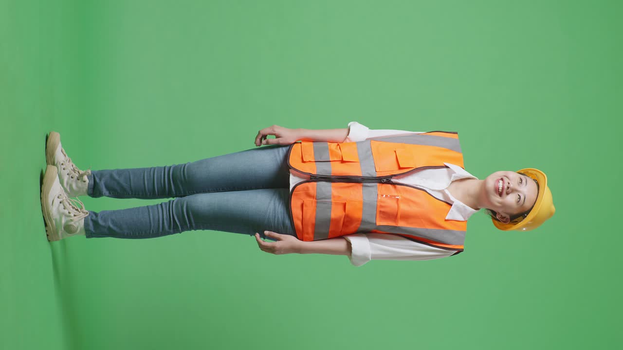 vista lateral completa del cuerpo de una ingeniera asiática con casco de seguridad mirando a su alrededor mientras está de pie en el estudio de fondo de la pantalla verde